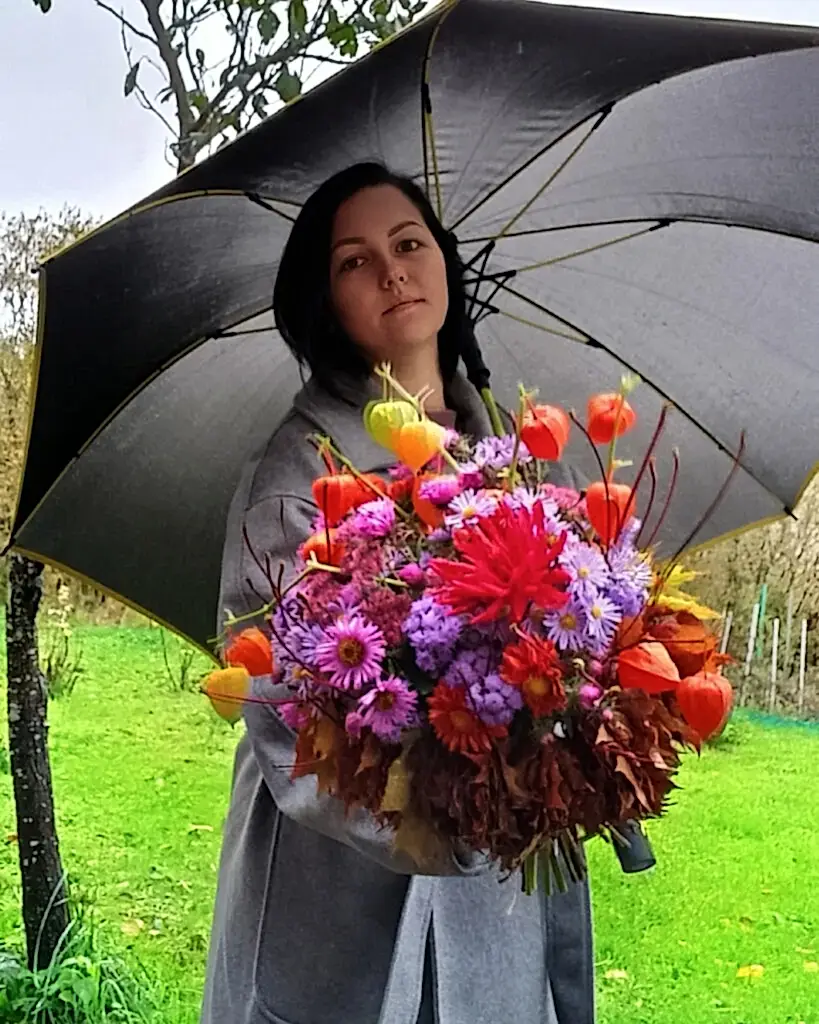 Женщина с зонтом держит осенний букет.